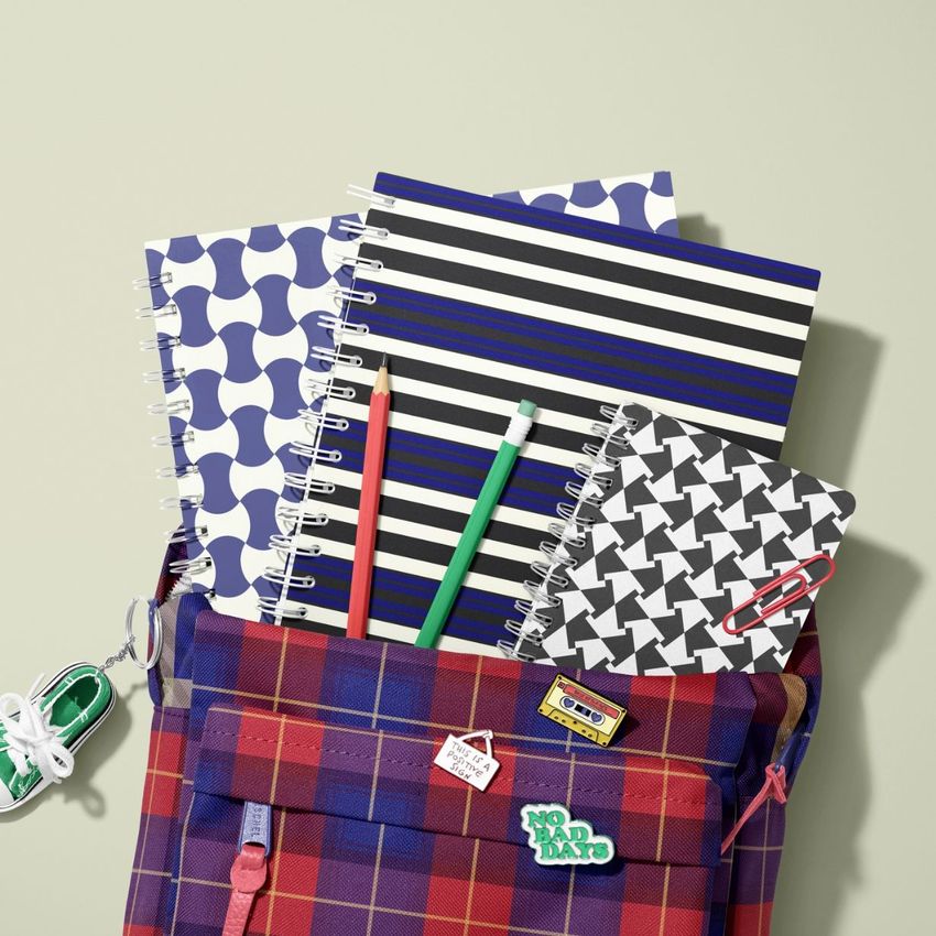 School backpack mockup with a red and blue tartan pattern, filled with spiral notebooks featuring geometric covers and two pencils.