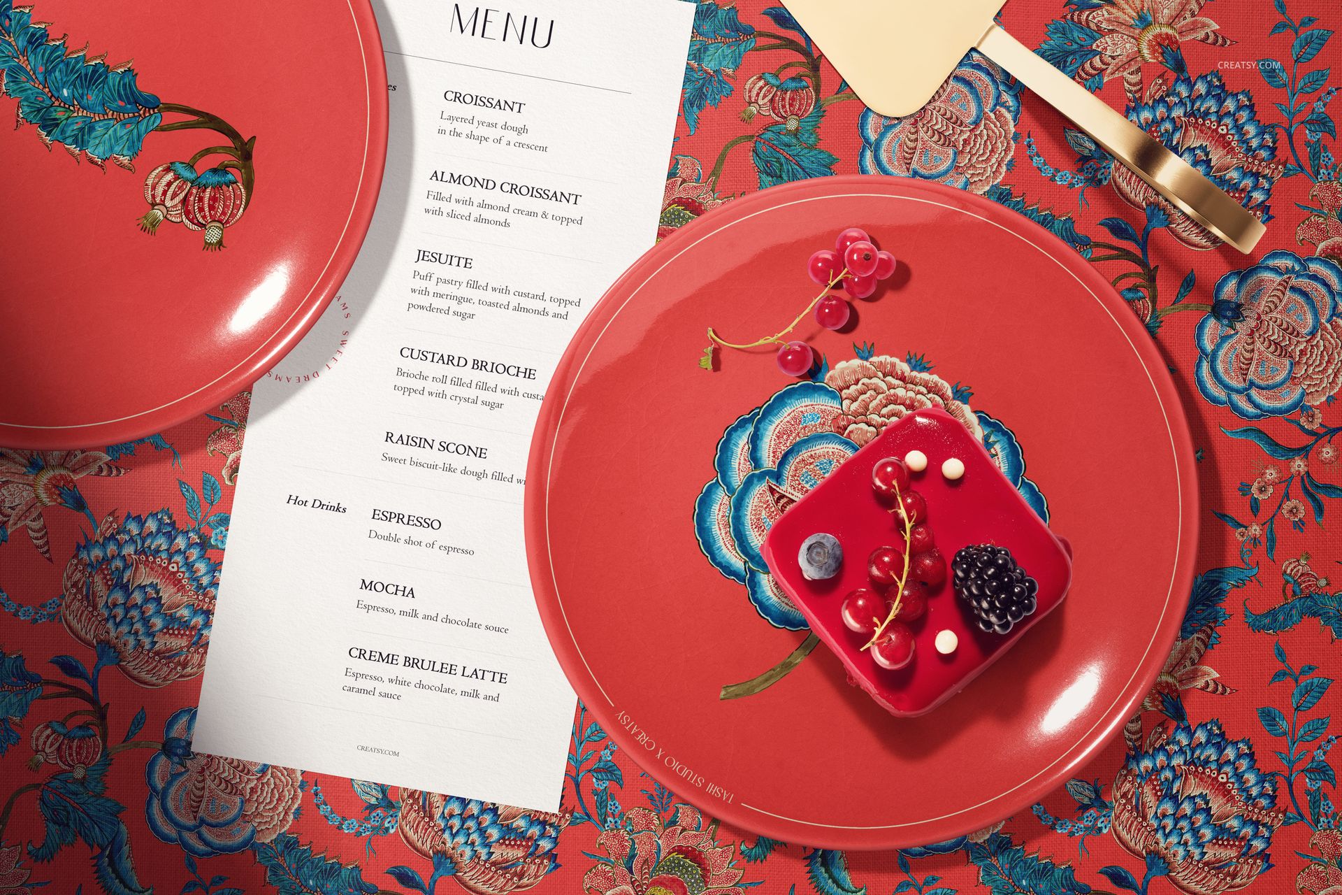 Floral ceramic plates mockup featuring a red color scheme, dessert, gold cake server, and a menu on a patterned fabric.