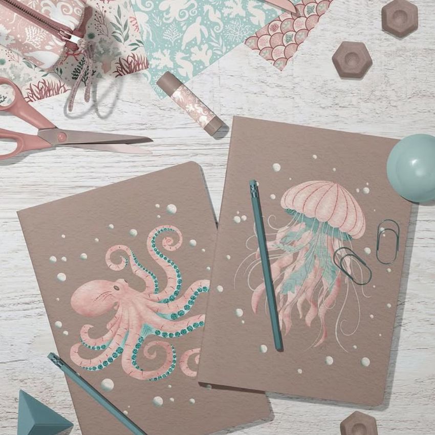 Stationery mockup featuring two classic A4 notebooks with pastel sea creature illustrations, surrounded by office supplies on a white wooden surface.