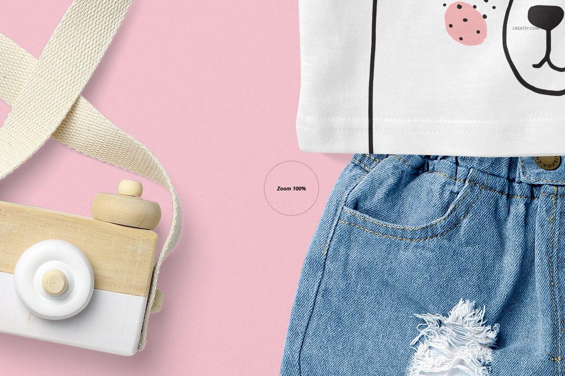 Close-up of a baby tank top mockup with a bear face print, paired with denim shorts and a wooden toy on a pink background.