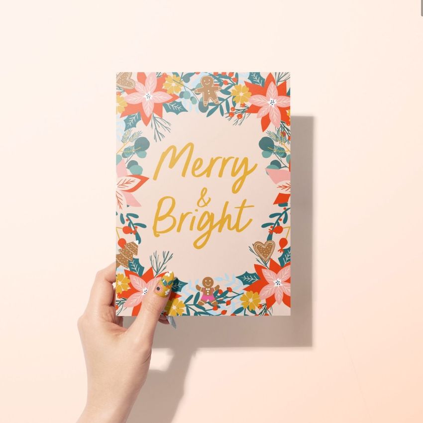Greeting card mockup featuring a woman's hand holding a card with colorful floral and holiday elements on a light background.