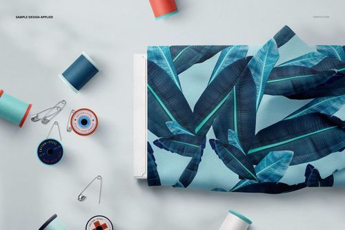 Fabric bolt featuring a tropical blue leaf design, placed next to assorted thread spools and safety pins in a mockup scene.