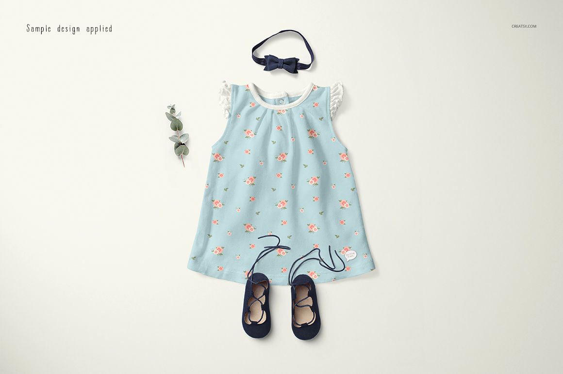 Front view of a baby dress mockup with a light blue floral pattern, paired with navy shoes and headband on a light background.