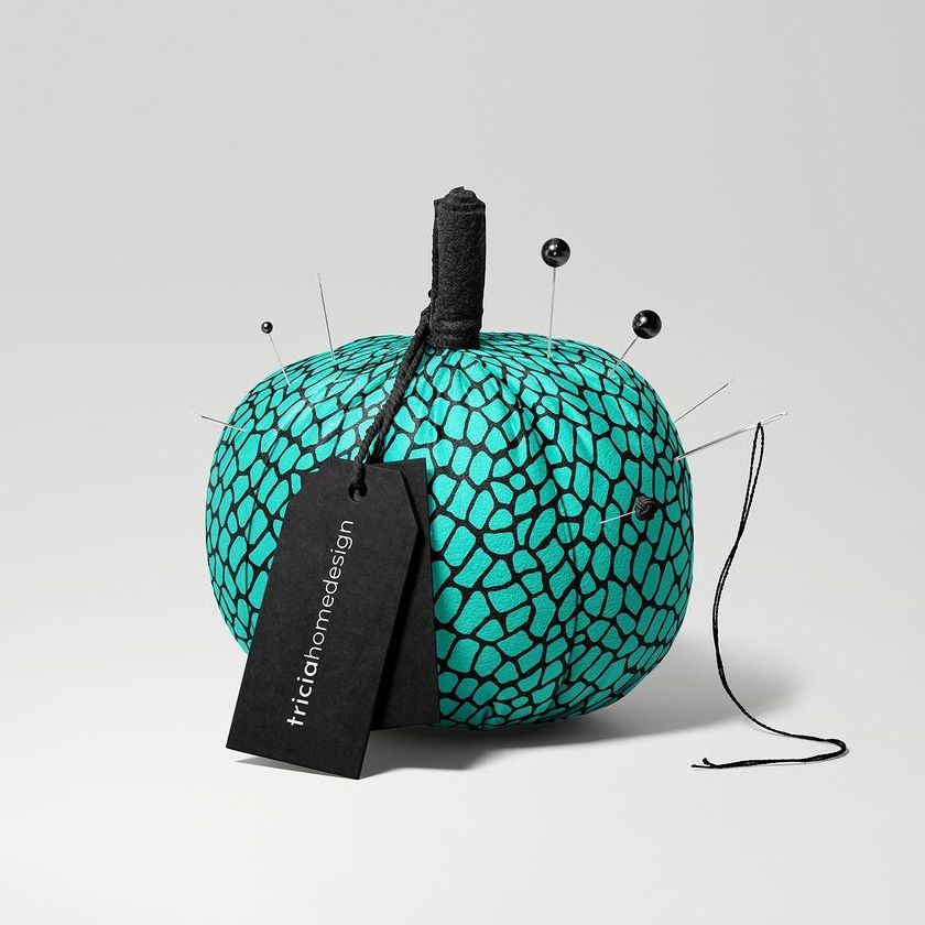 Fabric pumpkin mockup with a teal and black geometric pattern, black pins, and a black tag on a light gray background.