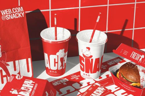 Fast food restaurant branding mockup featuring red and white cups with straws, burger, paper bag, and wrappers on a table.