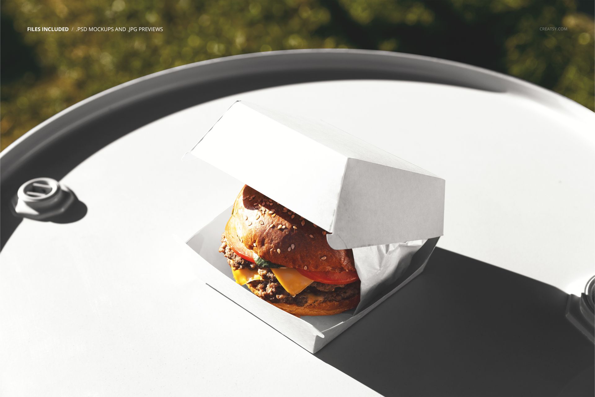 Burger box packaging mockup featuring a white box with a burger inside, displayed on a round gray barrel in sunlight.