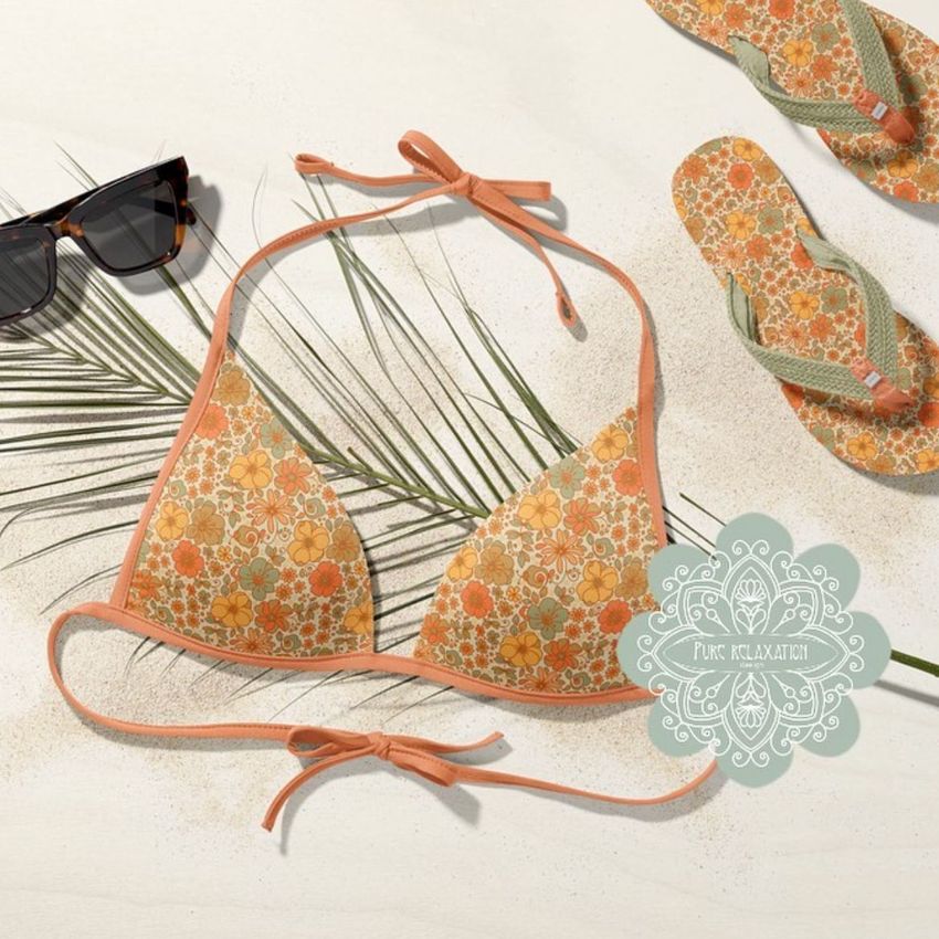 Bikini mockup set featuring a floral-patterned bikini top and bottoms laid on sand with sunglasses, palm leaves, and flip-flops.