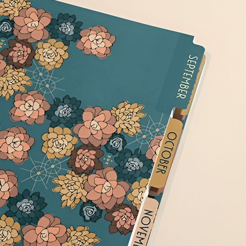 Planner mockup showing a closeup of divider tabs labeled September, October, and November with a floral cover design.