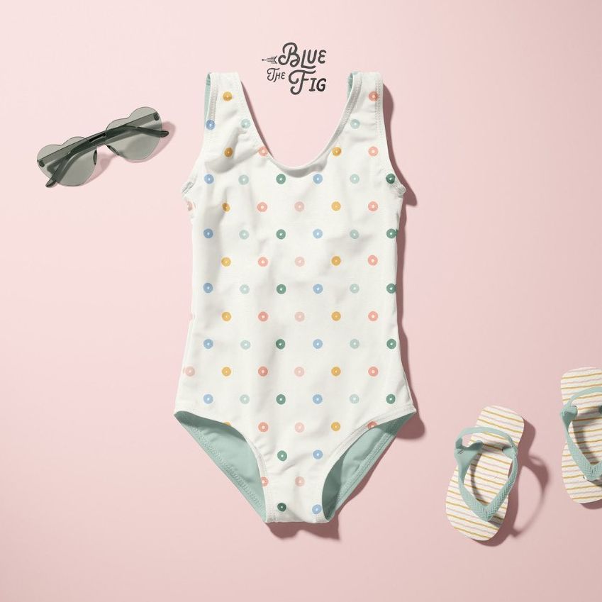 Baby swimsuit mockup displayed on a pastel pink background with colorful polka dots, sunglasses, and striped flip-flops.