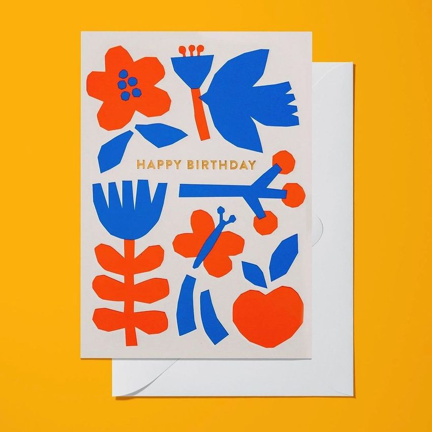A5 card mockup featuring a birthday card with bold red and blue abstract floral shapes and gold text on a white background.