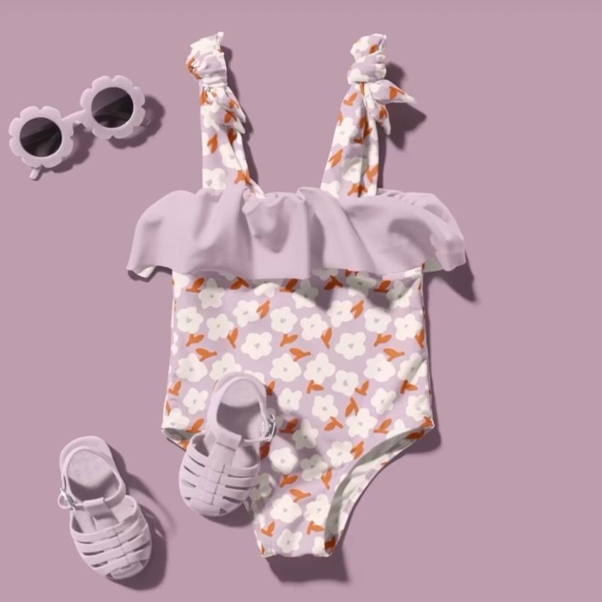 Baby swimsuit mockup with a floral pattern, matching sandals, and flower-shaped sunglasses on a pastel purple background.