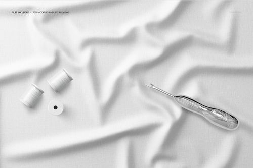 White creased fabric mockup with two spools of thread and a seam ripper, viewed from above on a flat surface.