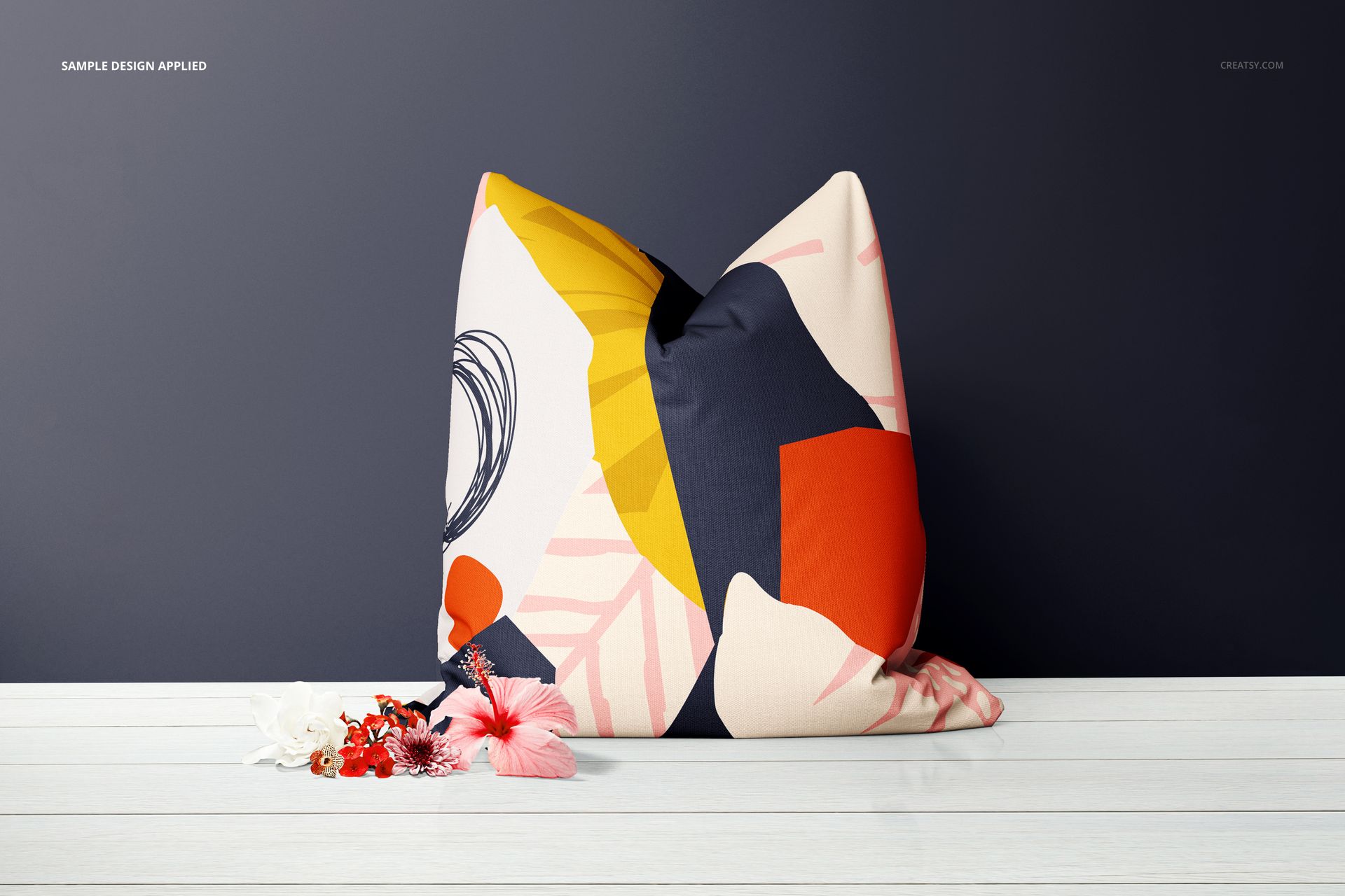 Front-facing decorative pillow mockup with bold abstract shapes, placed against a dark wall and white floor.