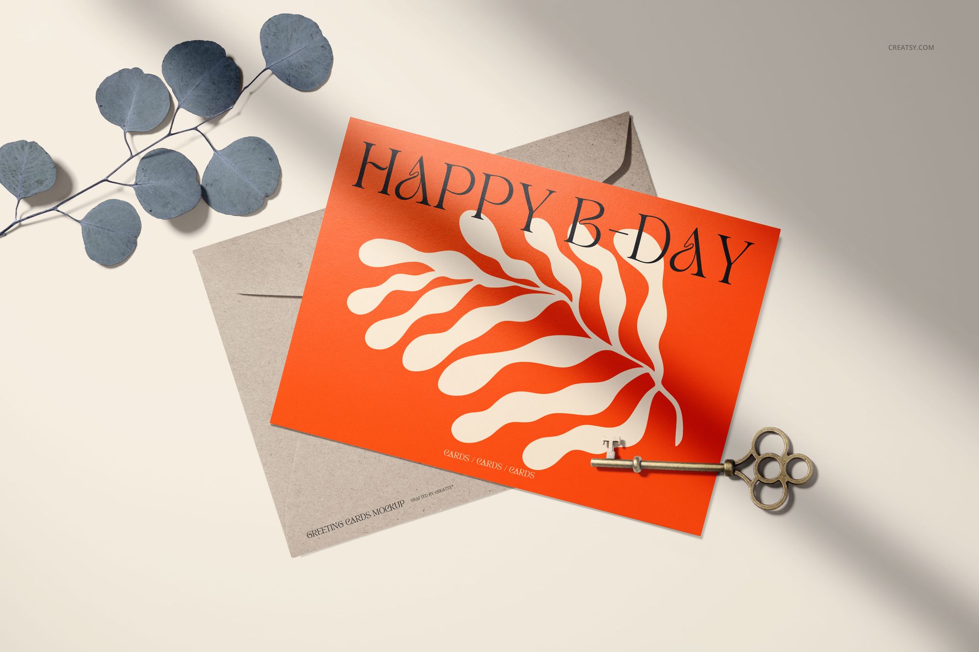 5x7 greeting card mockup featuring bold orange and white artwork, set atop a kraft envelope with a metal key and blue leaves.