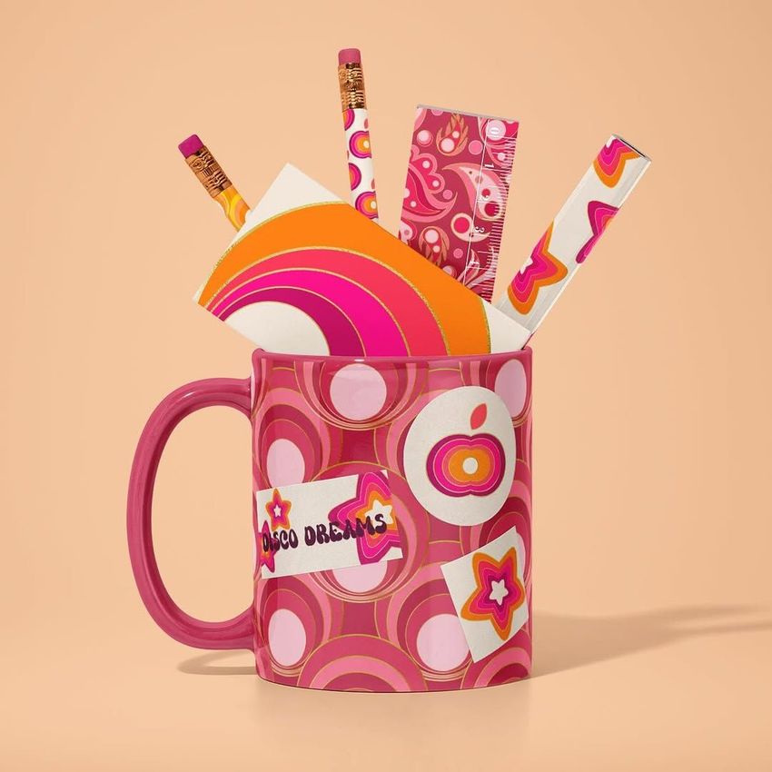 Mug mockup with a pink retro pattern, filled with colorful stationery items like pencils, ruler, and envelopes on a peach background.