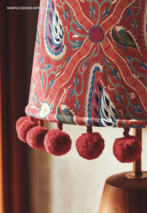 Detailed view of a velvet lampshade mockup with intricate multicolored design and red pom pom fringe.