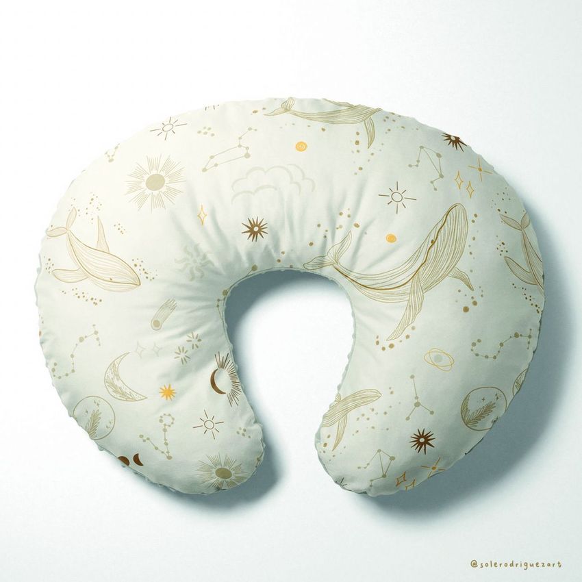 Boppy nursing pillow mockup with a light cream cover featuring gold zodiac-inspired patterns, whales, stars, and moons.