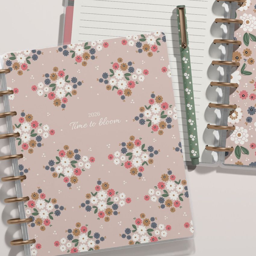 Two spiral-bound planner mockups seen from above, featuring pastel floral designs and a dotted green pen beside them.