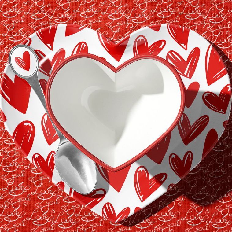 Heart-shaped cup mockup with red and white heart patterns, viewed from above on a red surface with handwritten text and a spoon.
