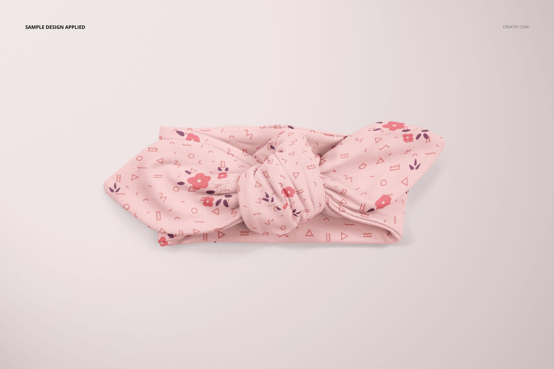 Top view of a soft pink baby headband mockup featuring a knotted center and scattered floral and geometric motifs.