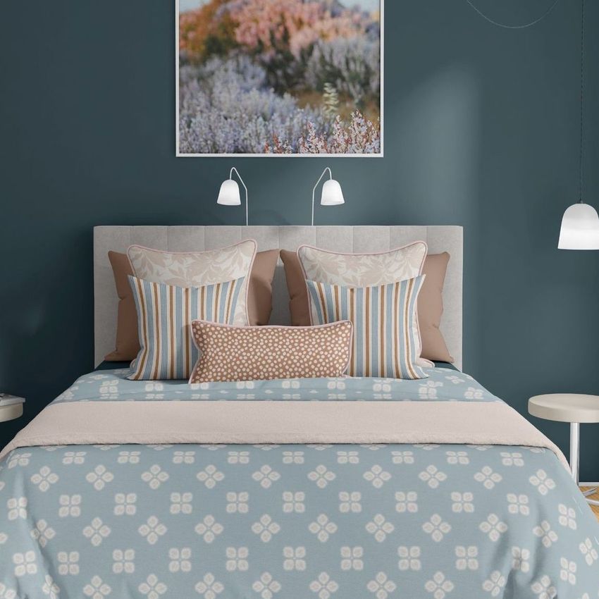 Bedroom scene bedding mockup showing a neatly made bed with patterned pillows and a blue duvet, set against a teal wall with a landscape photo above.