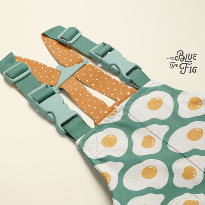 Kids rainwear mockup featuring green overalls with a fried egg pattern, mint green straps, and orange polka dot lining on a light background.