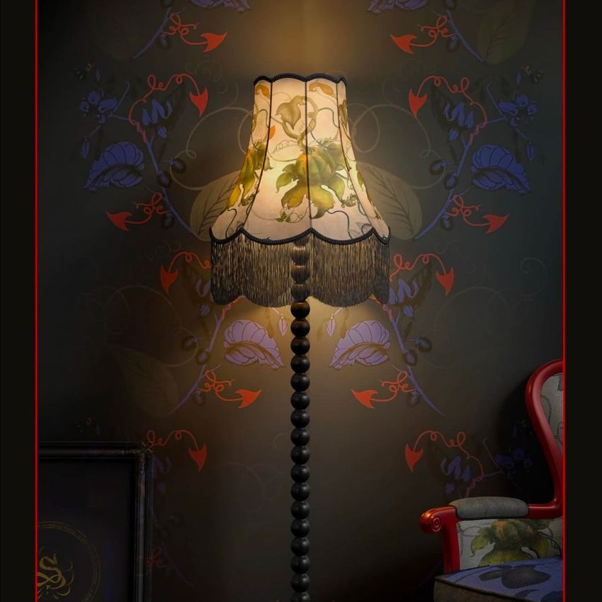Fringed velvet lampshade mockup displayed on a tall, ornate lamp with floral wallpaper and a patterned armchair nearby.
