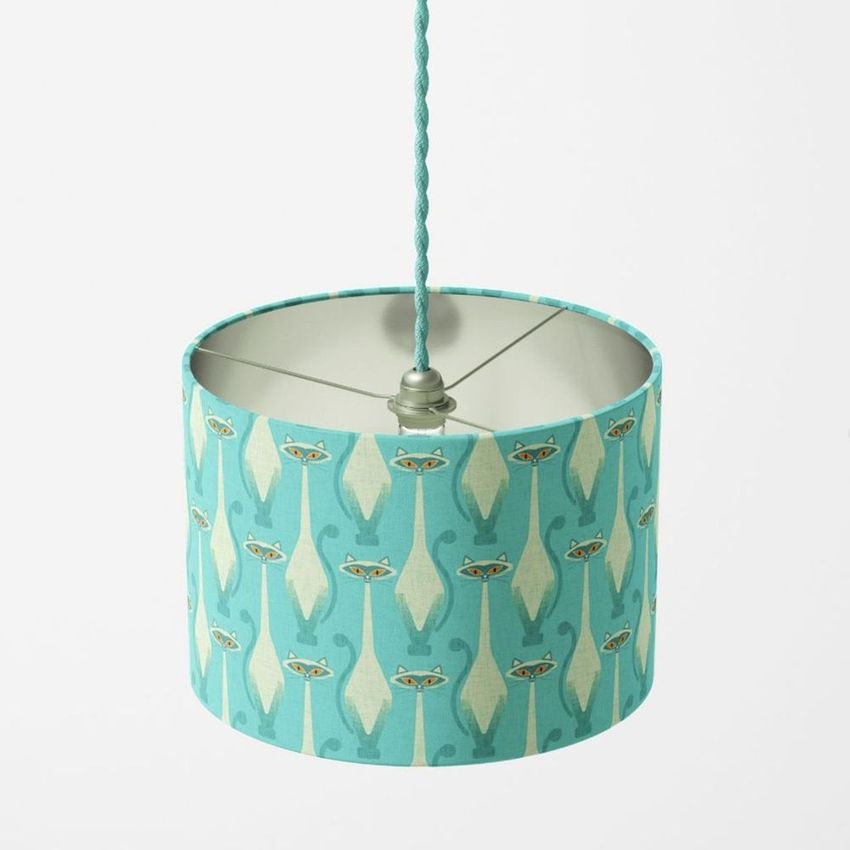 Drum lamp shade mockup featuring a turquoise fabric with a repeating pattern of stylized Siamese cats, suspended against a plain background.