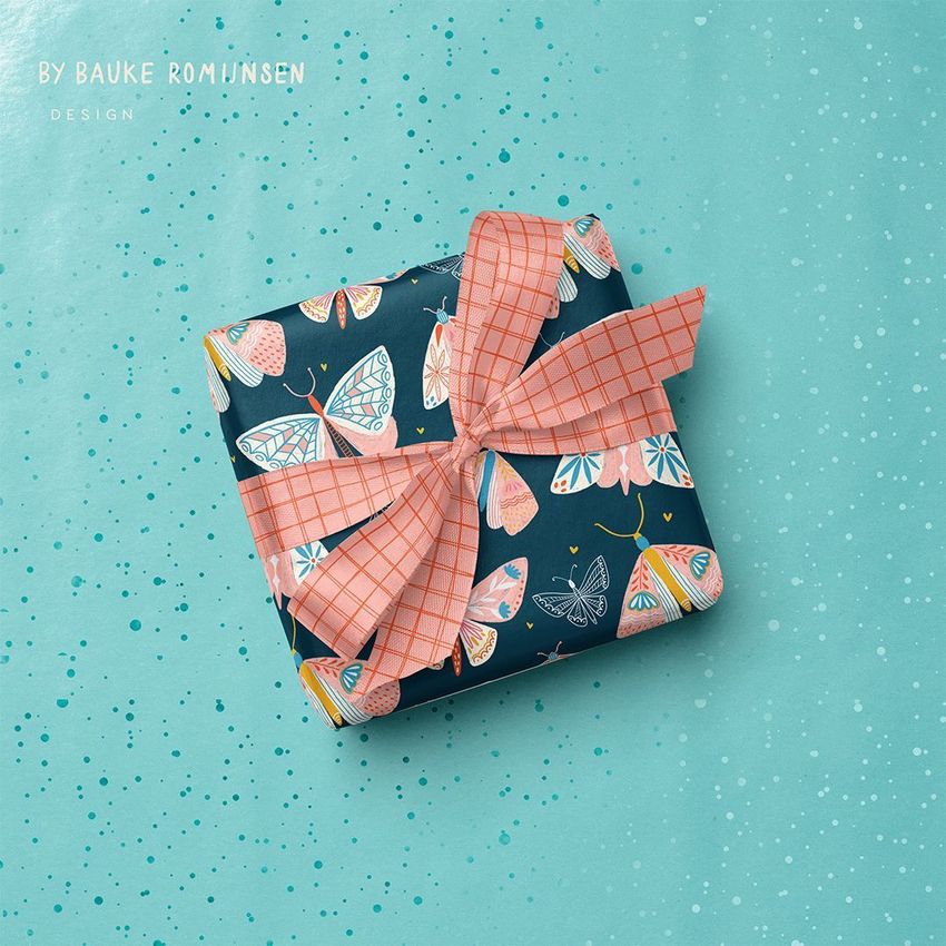 Square gift box mockup wrapped in dark paper with colorful butterfly and moth illustrations, topped with a pink plaid ribbon bow.