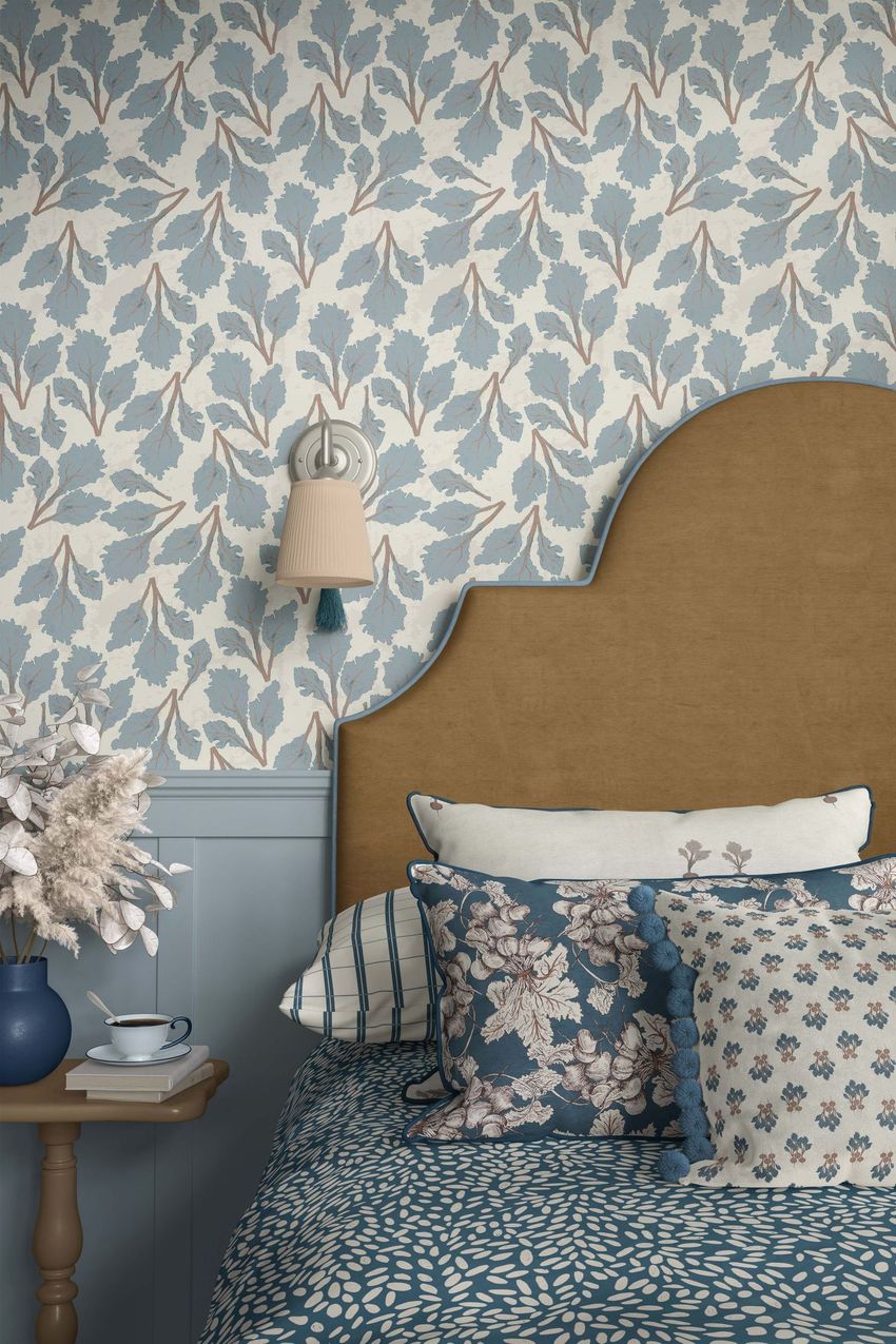 Bedroom mockup featuring a tan headboard, patterned pillows, and blue leafy wallpaper with a wall sconce above the bed.