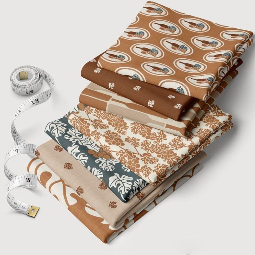 Fabric stack mockup featuring six folded textiles with Mediterranean-inspired patterns in earthy tones, placed on a white surface.