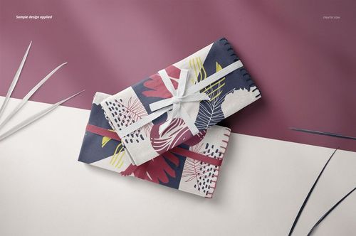 PSD mockup of folded linen fabrics with multicolored leaf motifs, displayed on a split burgundy and off-white background.