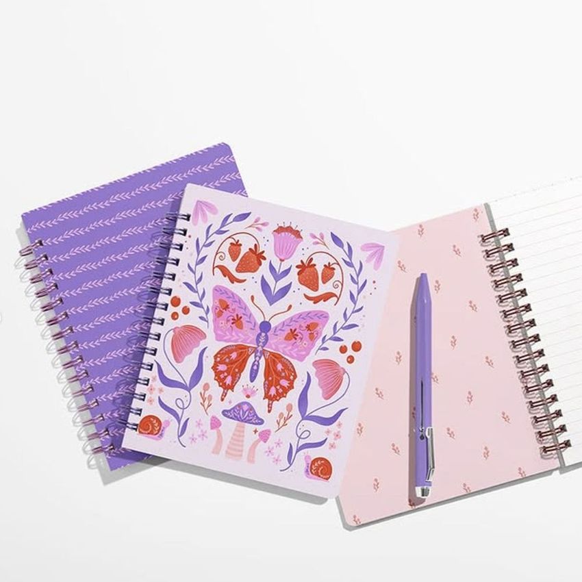 Coiled notebook mockup featuring three notebooks on a white surface, one with a colorful butterfly illustration, and a purple pen.