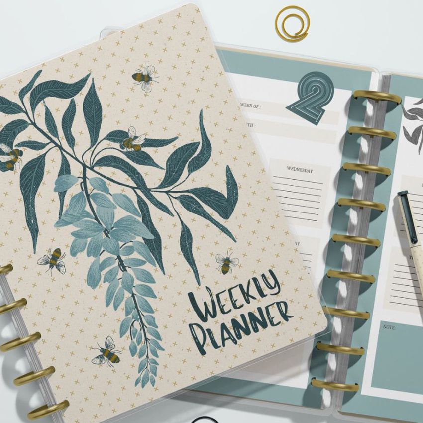 Top view of two spiral planners on a light surface, one closed with a botanical cover and the other open showing weekly pages.