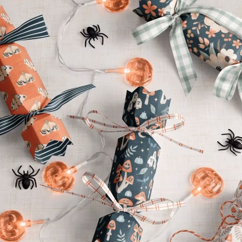 Halloween party cracker packaging mockup with patterned paper crackers in orange and navy, ribbon ties, and decorative spiders.
