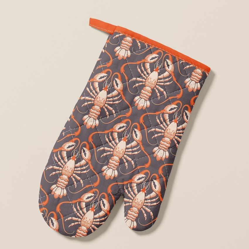 Oven mitt mockup featuring a repeating lobster pattern in red and white on a dark background, photographed on a light surface.