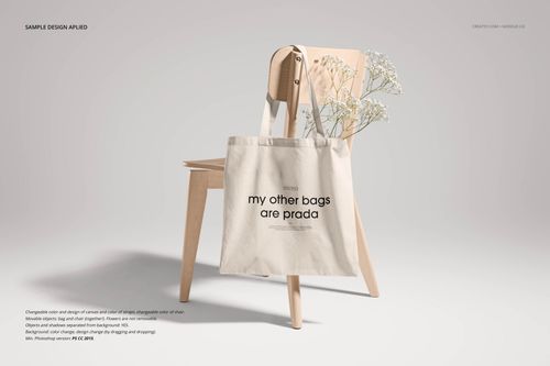 Neutral canvas tote bag mockup hanging on a light wooden chair, with white flowers in the background, front view.