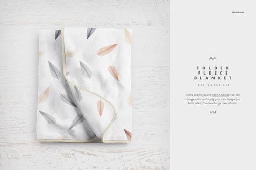 PSD mockup of a folded baby blanket featuring soft colored feathers, shown from above on a pale background.