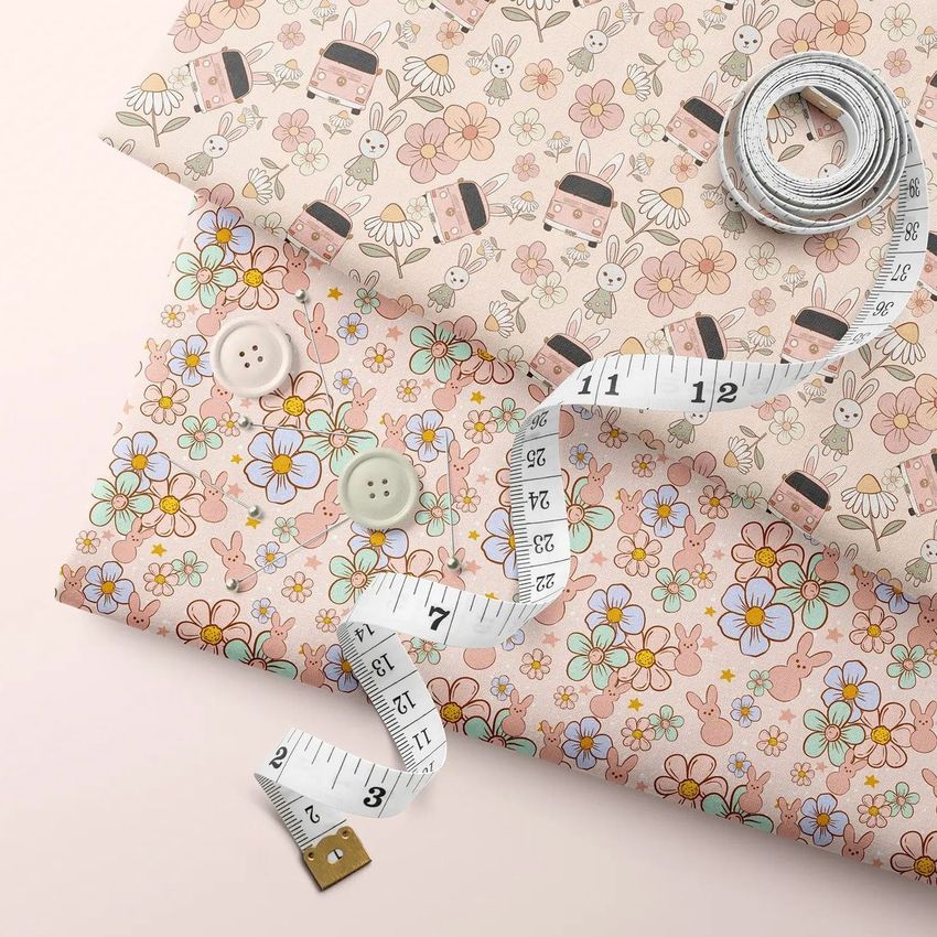 Folded fabrics mockup showing two patterned cloths with floral and bunny designs, a measuring tape, and buttons on a light surface.