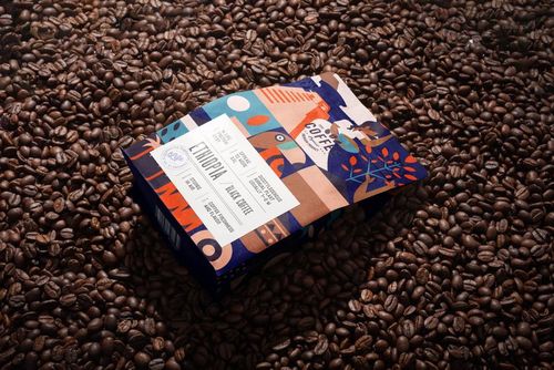 Coffee bag mockup featuring a vibrant geometric pattern and product label, displayed on a bed of roasted coffee beans.