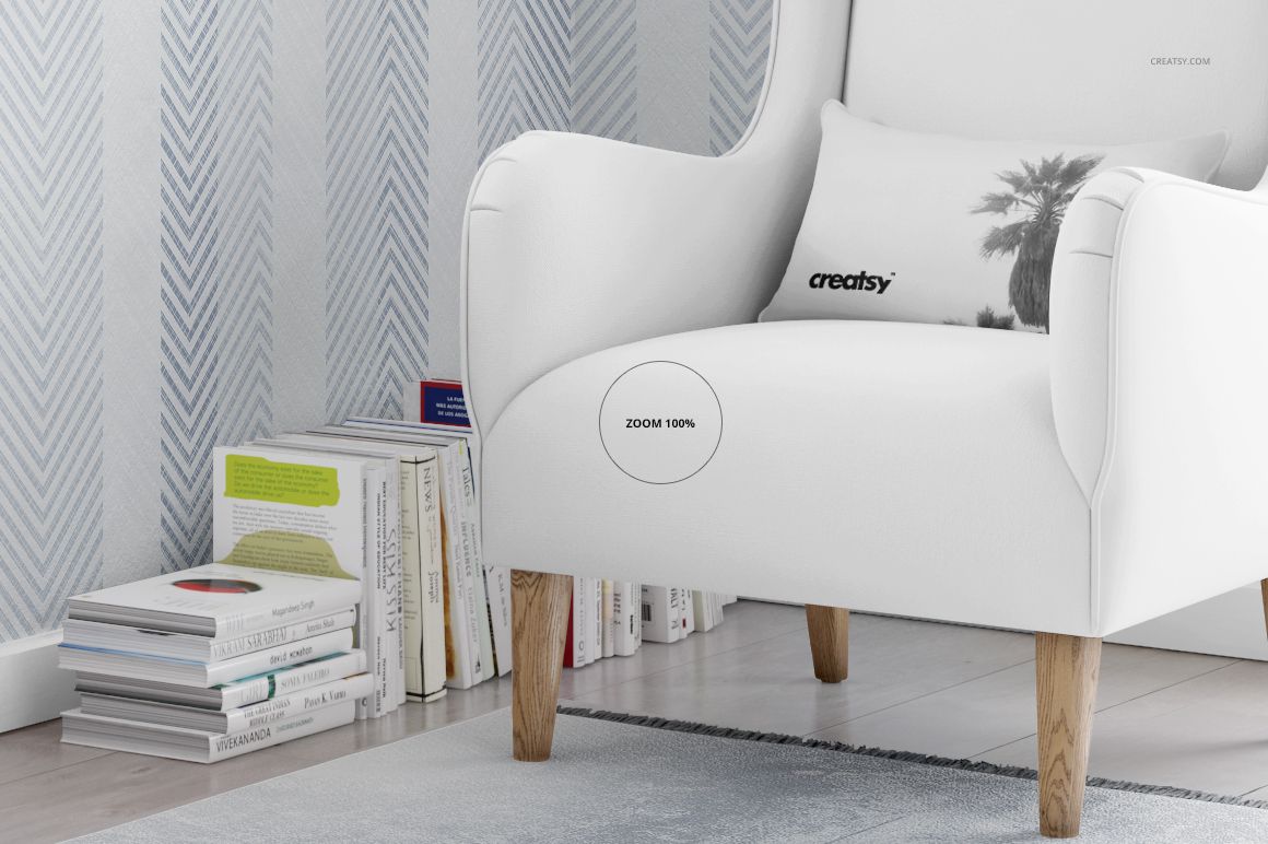 White armchair with wooden legs positioned on a light rug, next to a stack of books and patterned wallpaper background.