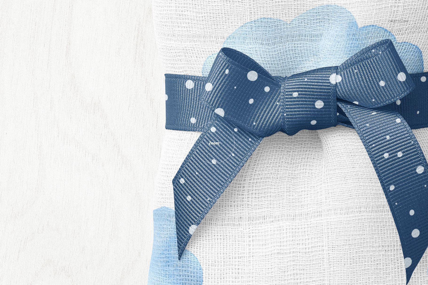 PSD mockup showing a baby muslin square nappy decorated with blue clouds and a textured blue bow, overhead perspective.
