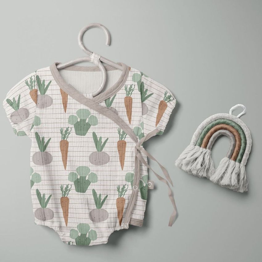 Muslin onesie mockup featuring a short-sleeve baby bodysuit with a vegetable pattern, displayed on a hanger next to a fabric rainbow decoration.
