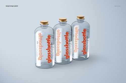 PSD mockup showing a trio of cylindrical glass bottles with bold orange text and natural wood caps on a pale surface.