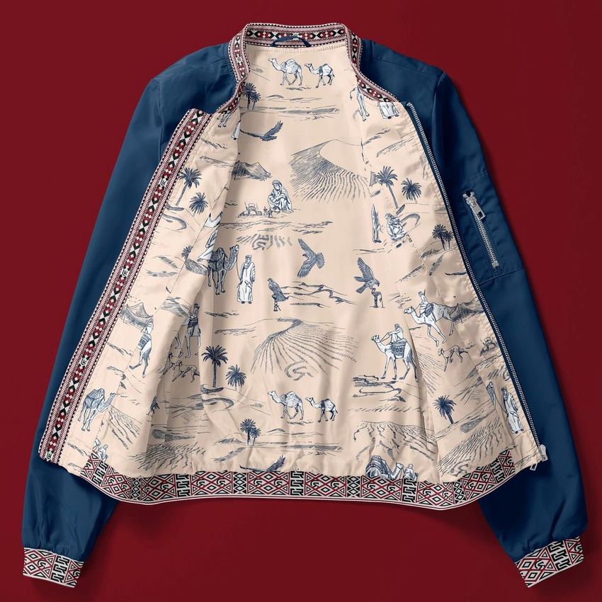 Women's bomber jacket mockup laid flat on a red surface, with the jacket open to reveal an illustrated desert scene lining.