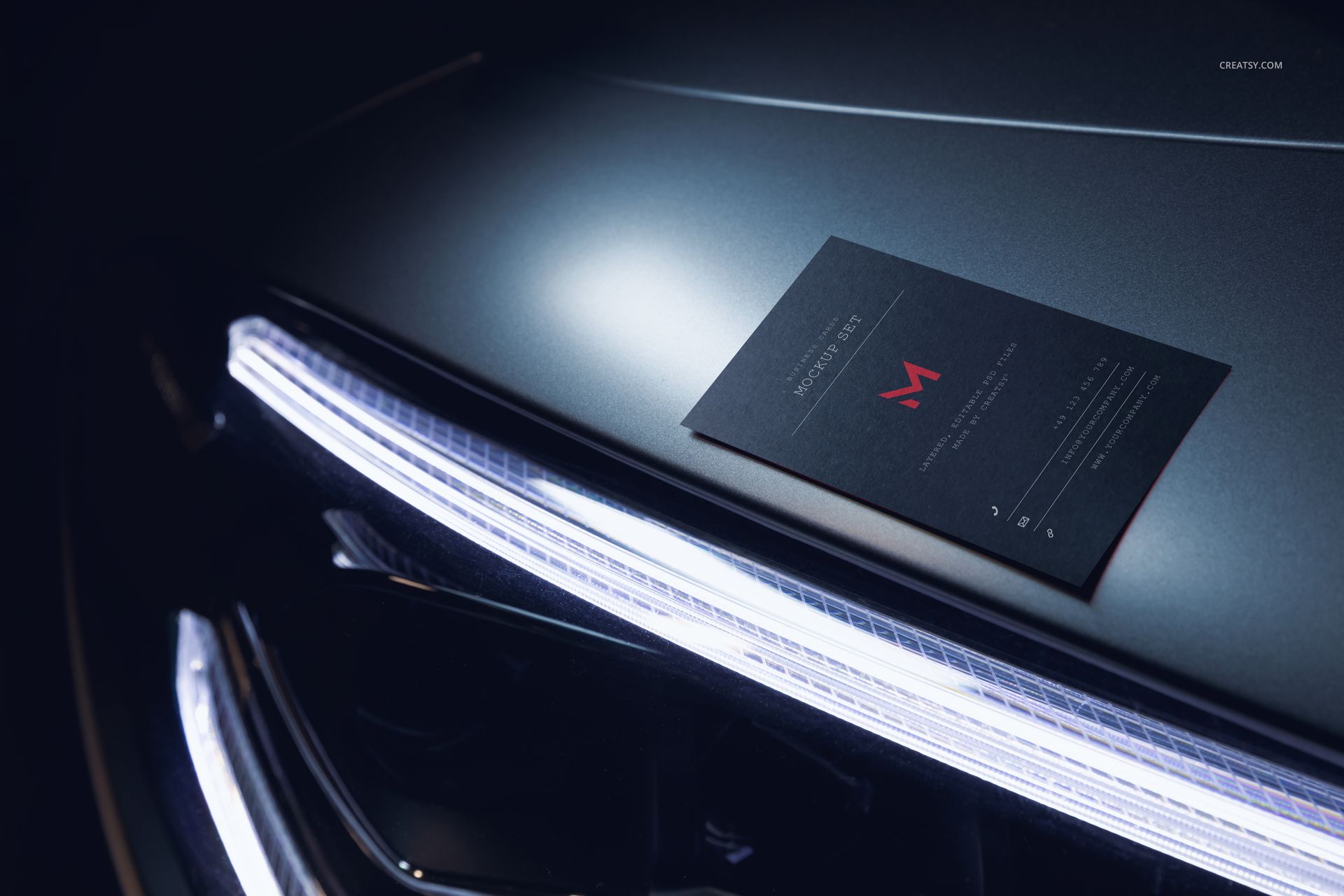 Automotive-themed business card mockup placed on a metallic car surface with bright LED light accents.