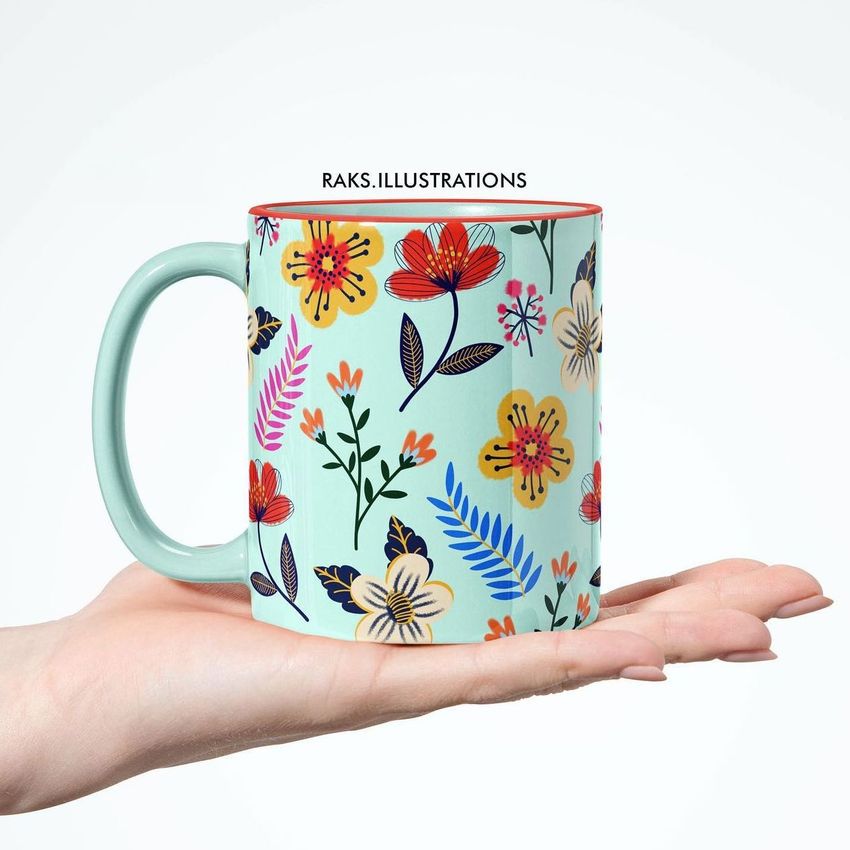 Mug mockup featuring a pastel green coffee mug with a colorful spring floral pattern, held in an open hand against a white background.
