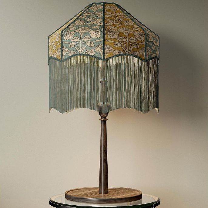 Table lamp mockup with a tassel shade featuring a floral pattern in muted green and gold, placed on a round glass table.