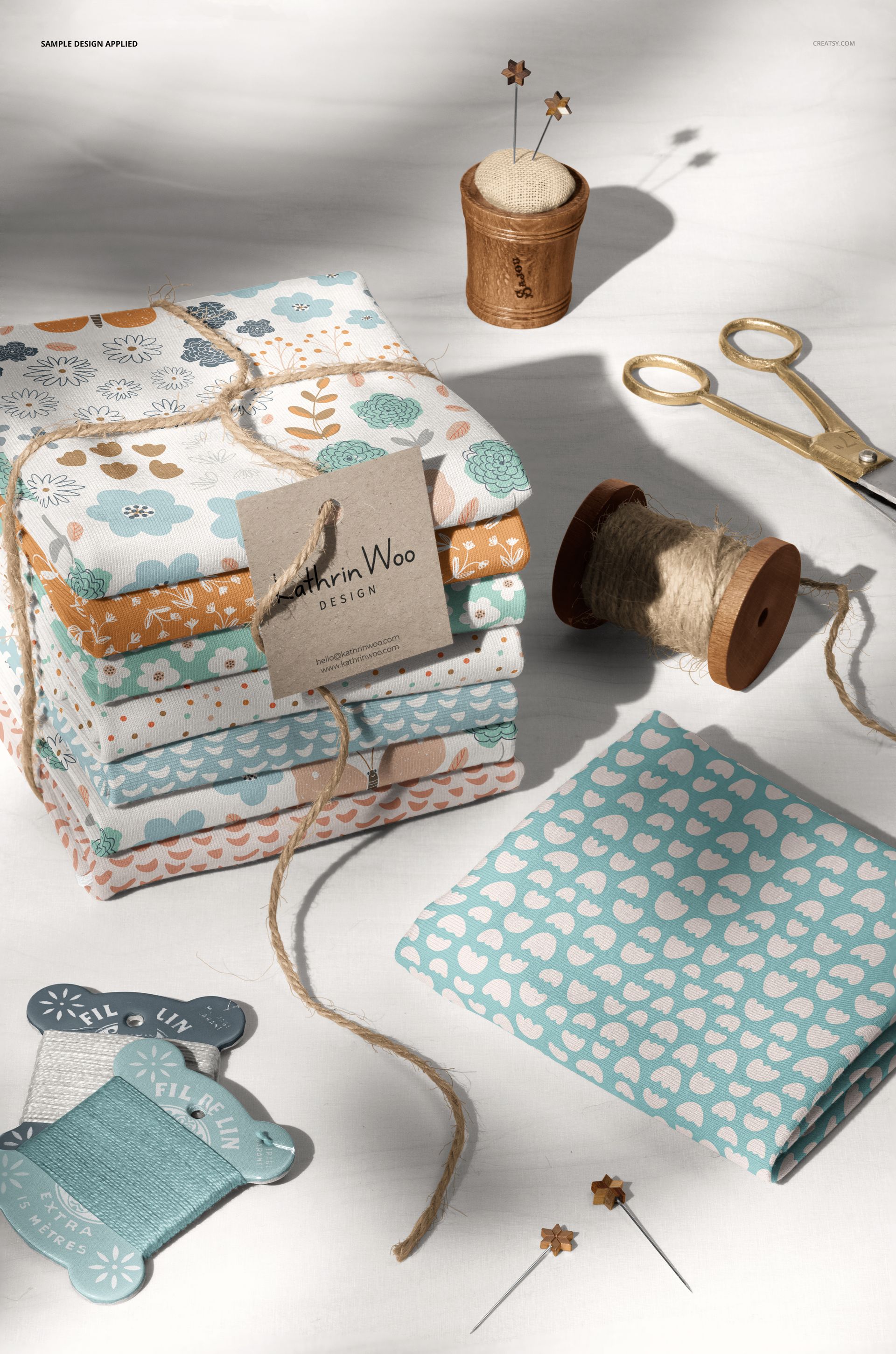 PSD mockup showing a pile of colorful jersey fabrics, a spool of thread, paper tag, and sewing accessories arranged neatly.