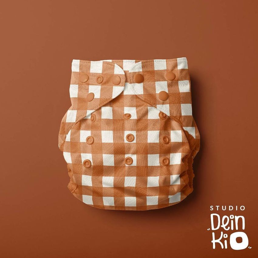 Reusable baby cloth diaper mockup with a brown and white buffalo check pattern, shown flat against a solid brown background.